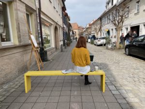 Petra Häfner sitzt auf der gelben Bank vorm Kreativlabor Erlangen in der Schiffstraße. Dort schreibt sie die gelbe Bank Kolumne.
