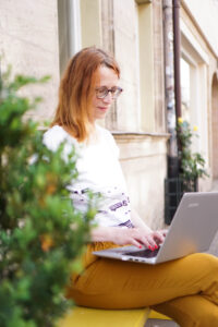 Petra Häfner sitzt auf der gelben Bank und schreibt auf ihrem Laptop